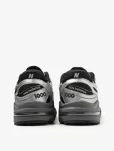 Zapatillas New Balance modelo M1000EGR, color plata y negro, con capellada de malla y revestimientos sintéticos. Cuentan con amortiguación ABZORB en el talón, Stability Web en el antepié, detalles reflectantes y logo 'N' engomado con contorno transparente.