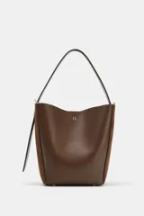 Bolso tipo saca con diseño estructurado, confeccionado en una combinación de cuero liso y gamuza en tono marrón. Cuenta con asa de hombro fija, cierre imantado y detalles metálicos en dorado.