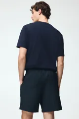 Pantalon corto de corte relajado color azul marino, confeccionado en tejido texturizado suave de mezcla de viscosa. Cuenta con cierre decorativo, cintura con elástico revestido y cordón de ajuste, bolsillos laterales discretos y bolsillo trasero insertado.