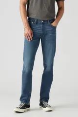Jean de corte slim fit con tiro bajo, confeccionado en denim azul con efecto de lavado desgastado. Presenta cierre de botones y remaches metálicos clásicos.