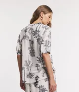 Camisa de viscolino Marfinno color beige con estampado de cocoteros en negro, cuello en V con escote hincapié y botones frontales negros. Mangas cortas con puños elásticos fruncidos.