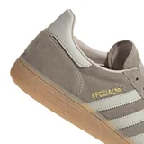 Championes adidas Handball Spezial inspirados en el modelo de 1979, confeccionados en gamuza gris topo con las clásicas tres tiras y refuerzo de talón en tono claro, inscripción lateral en letras doradas y suela de goma de tipo caramelo.