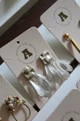 Aros colgantes plateados con base cuadrada texturizada y flecos de láminas metálicas.