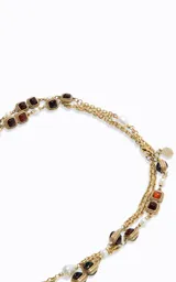 Collar largo de diseño en capas, elaborado en metal con acabado dorado. Presenta una estructura de cadena fina intercalada con aplicaciones de perlas blancas y piedras cuadradas en tonos rojizos y oscuros.