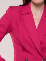 Blazer corto fucsia de corte entallado, con cuello solapa clásico, cierre frontal cruzado con doble botonadura a contraste, hombreras y mangas largas.