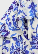 Vestido largo de corte evasé con estampado floral en tonos azules sobre fondo blanco. Presenta cuello de pico, tirantes con volantes y cierre de cremallera lateral.