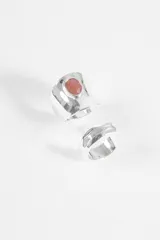 Set de dos anillos de metal plateado, uno de ellos con diseño liso y una piedra central de color rojizo, y el otro con textura irregular.