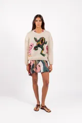Sweater de lana merino color beige, tejido a mano con diseño holgado, cuello redondo y bordados artesanales de ranas y detalles coloridos.