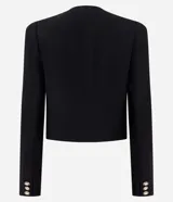 Chaquetilla ligera color negro de crepé de poliéster, con cuello redondo, manga larga y cierre frontal de botones dorados grabados. Cuenta con bolsillos frontales con solapa decorativa y botones a juego.