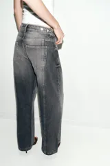 Jeans de tiro medio con diseño wide leg y cinco bolsillos. Presenta costuras verticales marcadas en el delantero y cierre frontal con cremallera y botón.