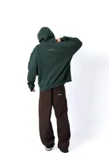 Hoodie de color verde oscuro confeccionado en friza, con capucha, cordones ajustables y bolsillo canguro. Presenta una estampa frontal blanca con el texto 'AnmeEdition' y 'CLUB' en un diseño ovalado de estilo desgastado.