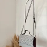 Cartera bandolera negra de ecocuero con diseño acolchado en rombos. Tiene asa corta superior y correa larga desmontable y regulable.