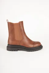 Bota Chelsea color marrón de cuero sintético, con elástico lateral, punta redonda y suela track color negro.