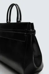 Bolso de mano de gran tamaño en color negro, con diseño estructurado, doble asa superior y cierre magnético. Incluye detalles de cintas laterales y compartimentos internos con cierre.