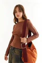 Top de manga larga color marrón, confeccionado en tejido acanalado con cuello bote. Presenta costuras decorativas expuestas a lo largo de las mangas, creando un efecto de relieve.