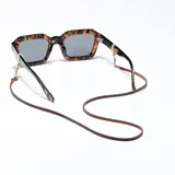 Correa para lentes marca Meller, confeccionada en cuero sintético color marrón con detalles metálicos en tono dorado. Incluye terminales de silicona ajustables para sujetar las gafas y un dije circular con el logo de la marca grabado.