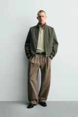 Pantalón de corte baggy fit confeccionado en tejido de algodón con estructura diagonal y efecto lavado. Presenta cintura con pliegues frontales, bolsillos laterales, bolsillos traseros de vivo y un bolsillo lateral adicional con doble vivo en la pernera. Cierre frontal con cremallera y botón.