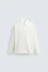 Camisa de corte relajado, color blanco hueso, con finas rayas verticales en tono grisáceo. Presenta cuello solapa, manga larga, bolsillo de parche en el pecho y bajo con aberturas laterales.