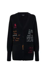 Cardigan negro de punto con escote en V y cierre frontal de botones. Presenta mangas tres cuartos y bolsillos frontales. El diseño destaca por sus bordados coloridos con motivos de cerezas y frases en francés distribuidas por toda la prenda.