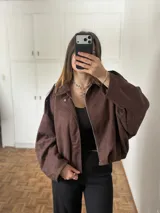 Campera de gamuza color chocolate, con corte oversize, cierre frontal y diseño de hombros caídos.