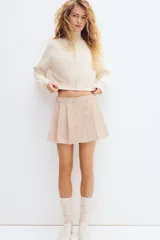 Short pollera de sarga color beige con diseño tableado, tira frontal con botones forrados decorativos y sutiles rayas finas.