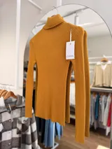 Polera de tejido de punto acanalado color mostaza, con cuello alto y mangas largas, de calce ajustado al cuerpo.