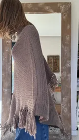 Poncho tejido en lana merino color marrón, con diseño de punto acanalado y terminación con flecos en el borde inferior. Incluye una pequeña etiqueta de cuero en la parte posterior.