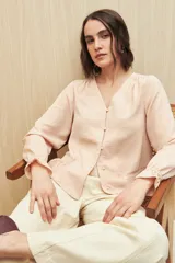 Camisa negra de manga larga con escote en V y botones forrados al tono en el frente. Destaca por su textura sutil y por el detalle de frunces con volados en la parte inferior.