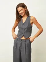 Chaleco de sastrería gris oscuro con diseño de rayas verticales finas, escote en V y cierre frontal con tres botones. Presenta un corte entallado y bolsillos decorativos en la parte inferior.