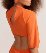 Vestido largo color naranja vibrante, con escote en V profundo que se anuda al frente, mangas amplias tipo mariposa y recortes laterales en la cintura.