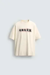 Camiseta relaxed fit color crema, con cuello redondo y manga corta. Presenta un estampado frontal con caracteres japoneses en negro y contorno rojo.