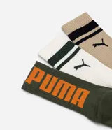 Kit de tres pares de medias deportivas Puma de caña larga, confeccionadas en algodón. Incluye un par blanco con rayas y logo azules, un par negro con rayas y logo blancos, y un par liso de color azul.