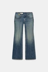Jeans de tiro bajo con corte bootcut, confeccionados en denim con efecto lavado. Presentan costuras verticales marcadas en el frente, cierre frontal con cremallera, gancho metálico y detalle de trabilla con botones en la cintura.