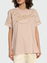 Remera de algodón color rosa pálido, con cuello redondo y mangas cortas. Presenta el logo de la marca bordado en el frente con un diseño de tipografía cursiva en hilo dorado.
