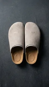 Zueco estilo sandalia de diseño cerrado, color beige, confeccionado en material texturizado con plantilla anatómica y suela plana. Presenta el logotipo de la marca grabado en la parte frontal.