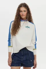 Sweater de punto color blanco con mangas raglán en azul y detalles en verde en los puños, cuello redondo y bordado de libélula en el pecho.