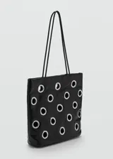 Bolso tipo shopper de color negro con diseño de ojales metálicos plateados. Cuenta con doble asa de hombro y cierre de botón magnético.