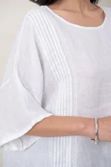 Blusa de lino color marrón oscuro, con escote redondo, mangas cortas amplias y detalle de alforzas verticales en el lateral derecho.