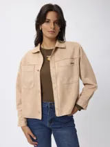 Campera de estilo camisero con efecto gamuzado, color beige, de corte recto y holgado. Presenta cuello clásico, cierre frontal con botones, mangas largas con puños abotonados y bolsillos frontales aplicados.