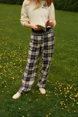 Pantalón largo de tejido suave con estampado a cuadros en tonos azul, marrón y blanco. Tiene elástico en la cintura, cierre decorativo con botones y bolsillos laterales.