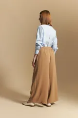 Pantalón ancho color tostado, de silueta fluida y cintura elastizada. Presenta una pretina ancha con botones metalizados irregulares.