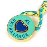 Llavero con dije circular de metal esmaltado en color turquesa, con un corazón azul en el centro y la inscripción 'EXTRA LARGE' grabada. Incluye una cuerda trenzada multicolor y herrajes dorados.