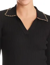 Buzo de tejido acanalado marca Rio & Rian, color negro, con cuello solapa decorado con una cadena metálica y escote en V. Presenta mangas tres cuartos y un ajuste al cuerpo.
