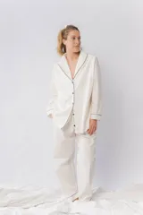 Pijama de dos piezas confeccionado en popelina de algodón color crema. Camisa de manga larga con cuello smoking, cierre frontal abotonado y detalles de vivo en contraste en cuello, puños y solapas. Pantalón de corte recto con cintura elástica, bolsillos laterales y detalle de vivo en el ruedo.