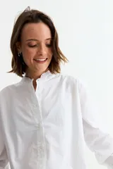 Camisa de manga larga color blanco, con cuello mao y puños con detalle de volados. Presenta cierre frontal con botones y un corte clásico.