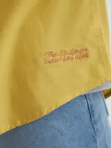 Camisa manga larga amarilla de algodón con bolsillo en el pecho, botones de pasta, logo bordado en el ruedo y etiqueta de marca en la tapeta de botones.
