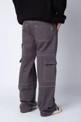 Pantalón tipo carpintero de corte relaxed fit y tiro medio, confeccionado en denim negro con costuras a contracolor en blanco. Presenta múltiples bolsillos cargo laterales, un bolsillo con cierre en la parte inferior y presillas utilitarias.
