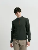 Sweater de punto color verde oliva, con cuello alto y medio cierre frontal. Presenta coderas en símil nappa y puños acanalados.