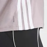 Remera deportiva Adidas de entrenamiento, color lila, con cuello redondo y mangas cortas. Presenta el logo de la marca en el pecho y las icónicas tres rayas blancas en los laterales. Diseñada con tecnología de absorción de sudor y ajuste clásico.