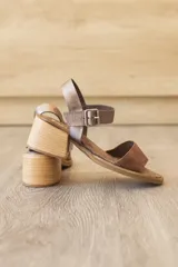 Sandalia de cuero marrón con tira frontal en cuero y correa al tobillo metalizada con hebilla ajustable. Cuenta con tacón ancho y bajo de acabado símil madera.